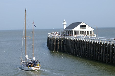ein Segelboot fährt am Oosterstaketsel mit weißer Brasserie vorbei.